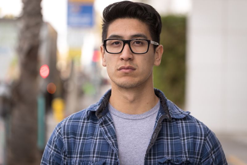 serious young hispanic man wearing glasses in the street